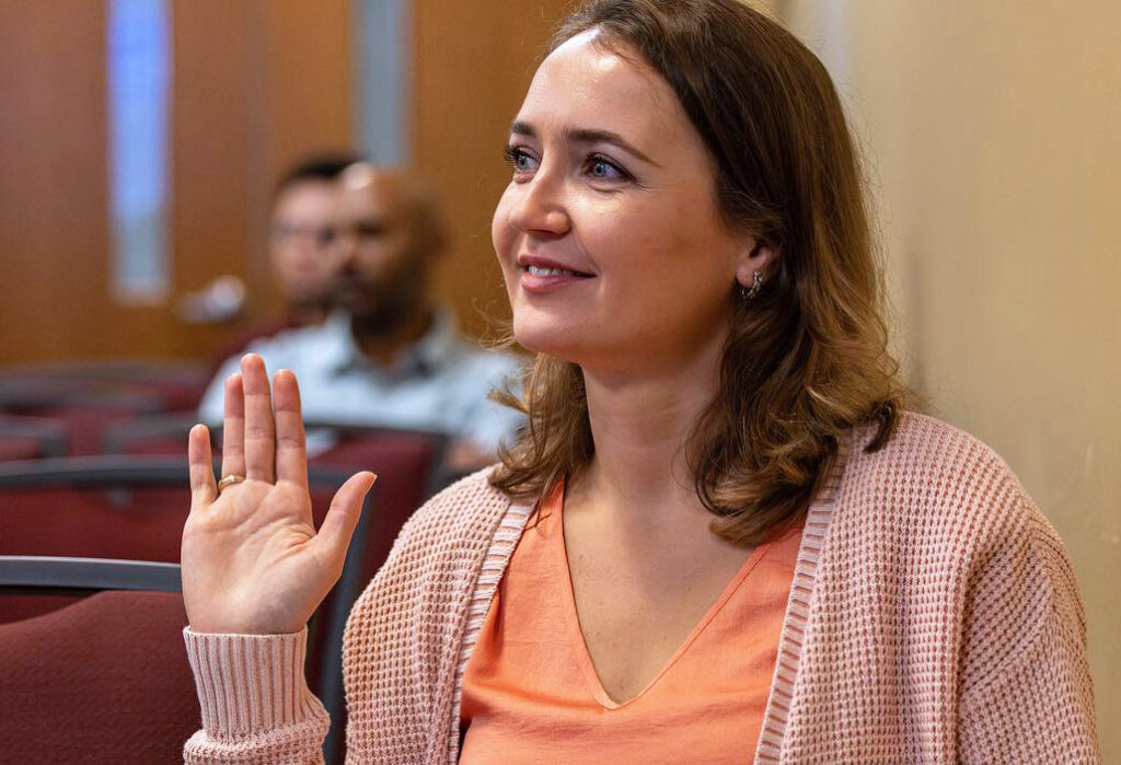 A female postdoctoral researcher raising her hand during a symposium presentation