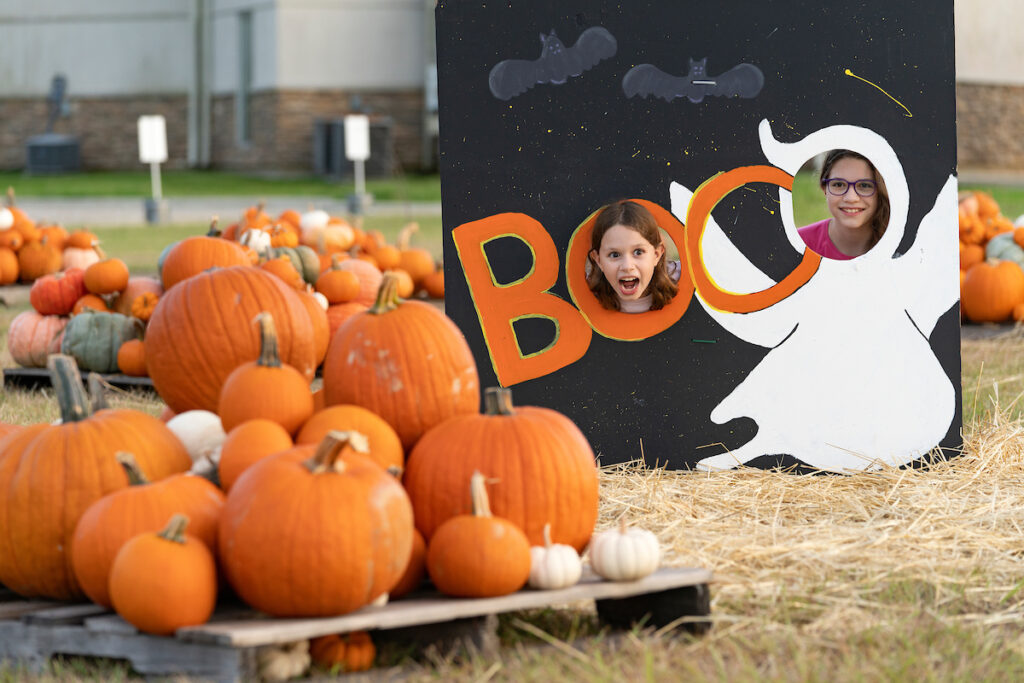 Two children poke their heads through a standing cardboard image that says Boo