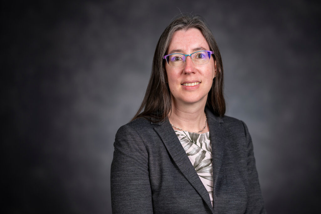 Headshot of Ann Wehman, Ph.D., in front of a gray background. She is wearing a dark gray jacket