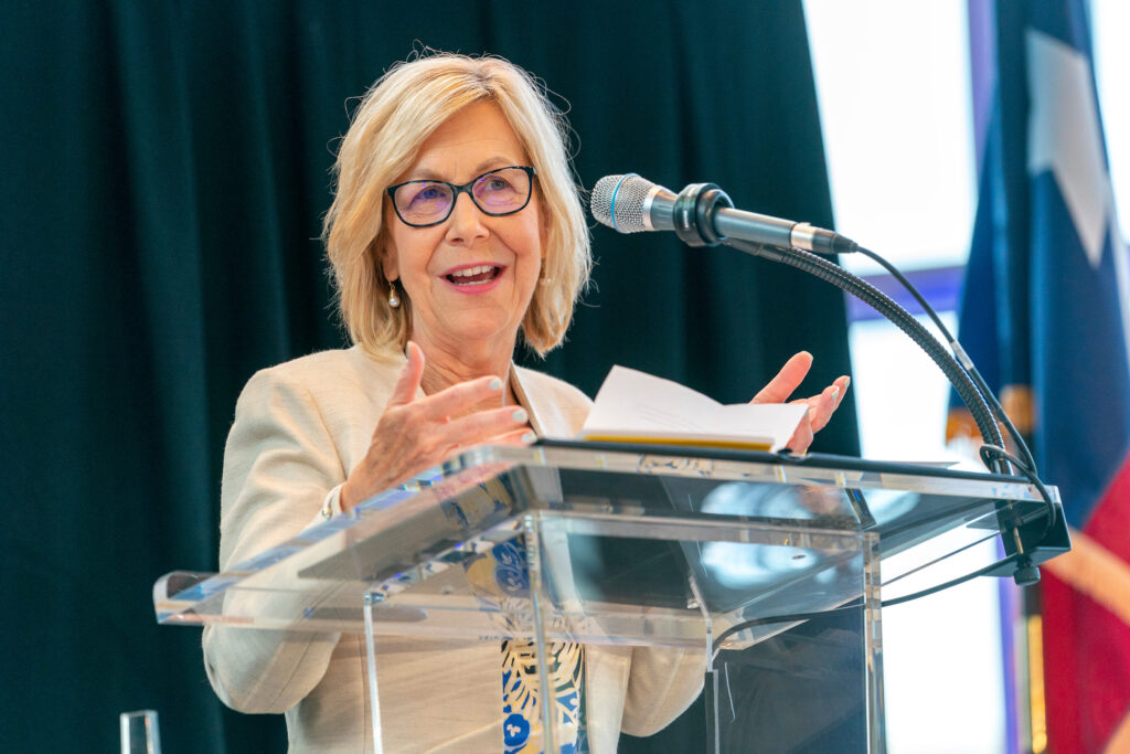 A woman stands behind a podium wile speaking at a podium onstage