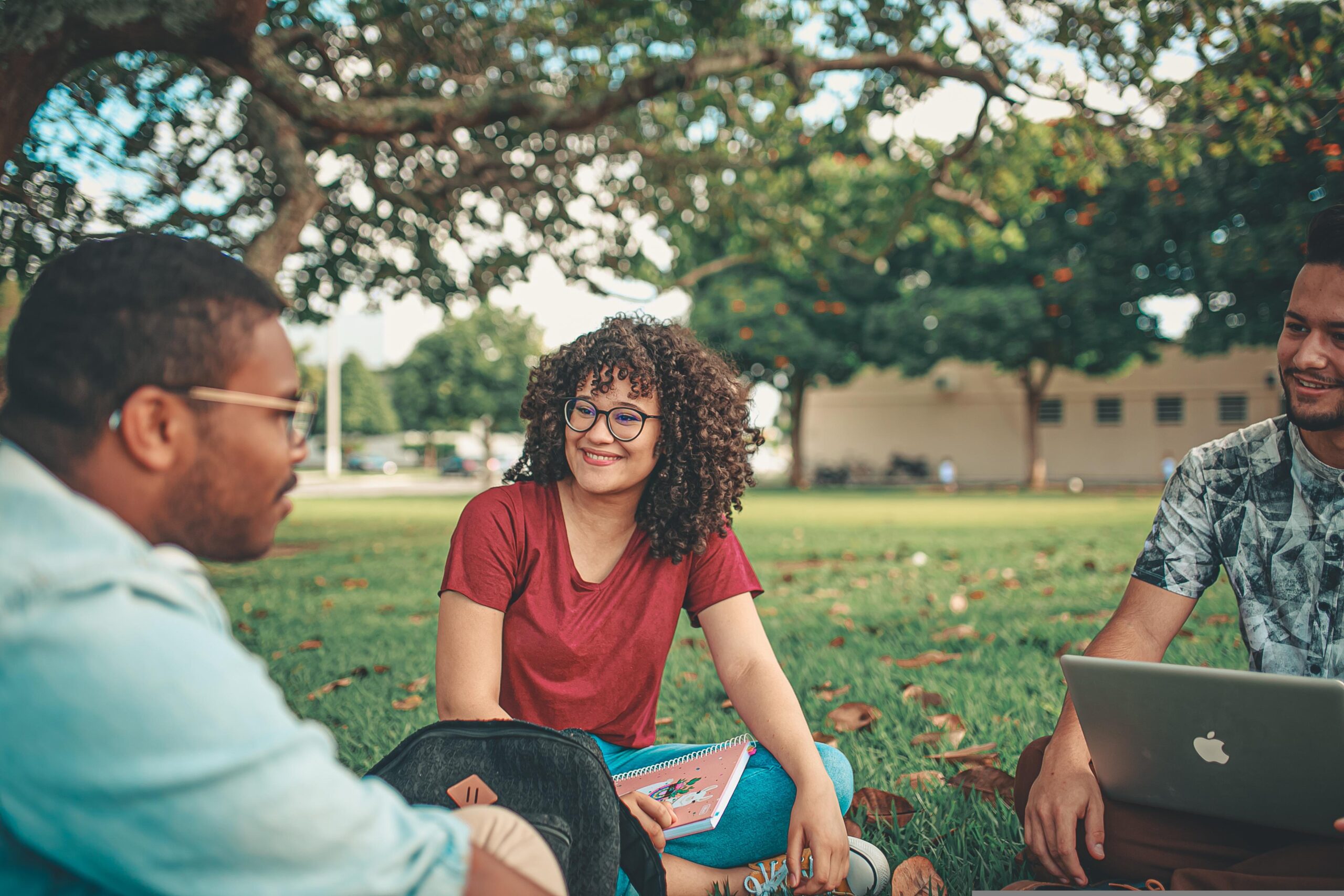 Students sitting on the grass under a tree smiling and talking