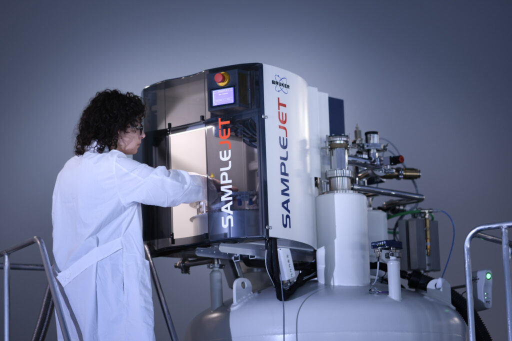 Researcher in a lab coat reaching inside of a SampleJet automation machine