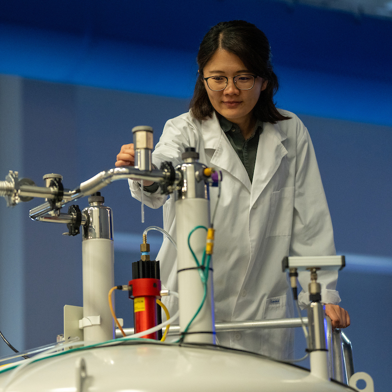 Student in a lab coat tinkering on lab equipment