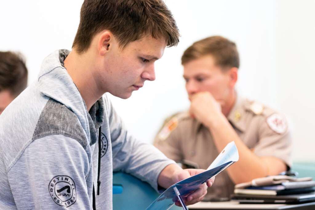 Close up of male student reading in classroom, with another student in the background.