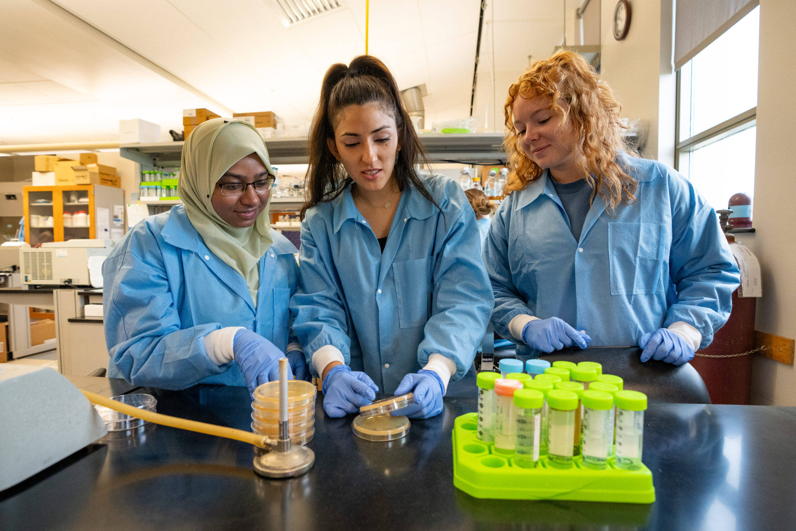 Students in blue lab coats examine a petri dish in a lab setting