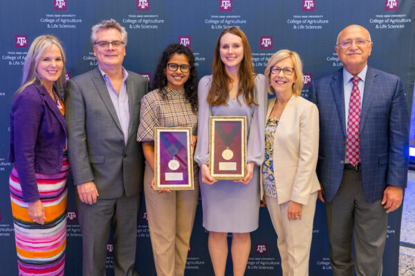 A group of six people standing and smiling, with two women in the center holding Early Career Awards.