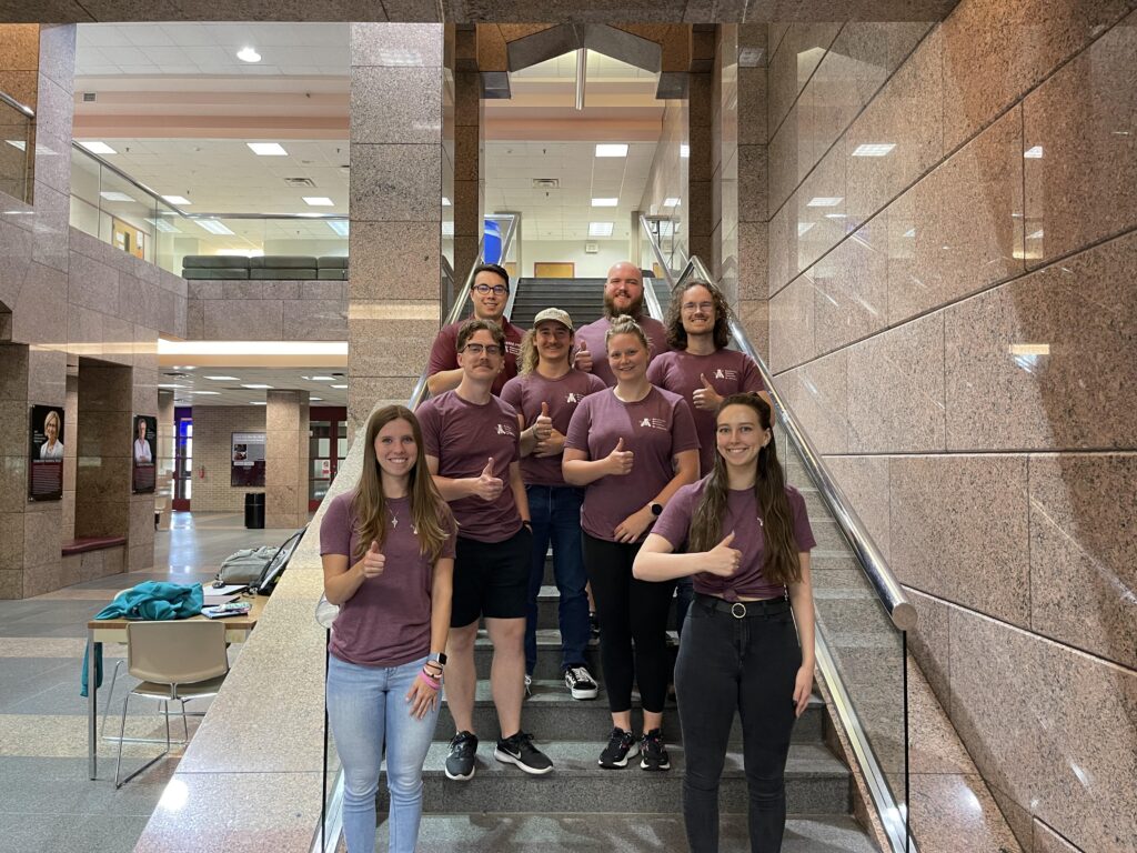 Biochemistry Graduate Association members standing on stairs and giving a thumbs up