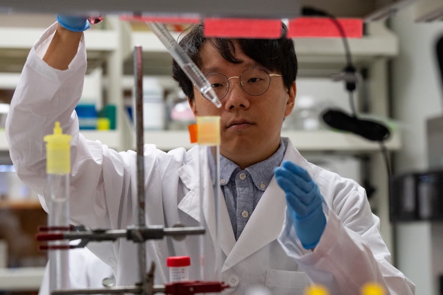 Researcher in a white coat pipetting a substance into a beaker
