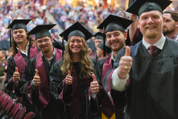 Aggies with graduation gowns pose with Gig 'Em thumbs