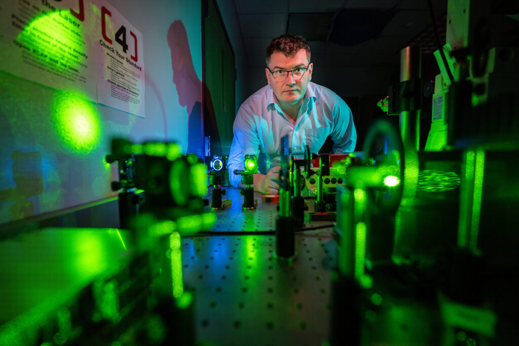 Kurouski leans over a lab bench covered in light-based sensors with green light